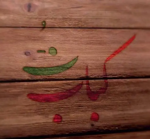 طرح هنری و خلاقانه نام کباب تُ به رنگ‌های سبز و قرمز بر روی سطح چوبی، نشان‌دهنده هویت بصری خاص رستوران کباب تُ.