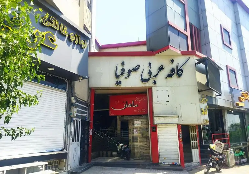 نمای خارجی کافه عربی صوفیا با ورودی اصلی، تابلوی ماهان، و حضور کسب‌وکارهای همسایه در یک خیابان پر جنب و جوش