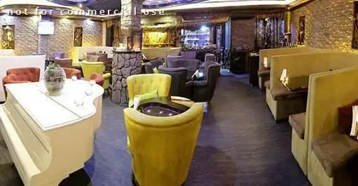 فضای دلنشین و دنج کافه رستوران دل فارو، شامل پیانوی سفید، مبلمان راحت زرد و بوث‌های شیک با دیوارهای سنگی.