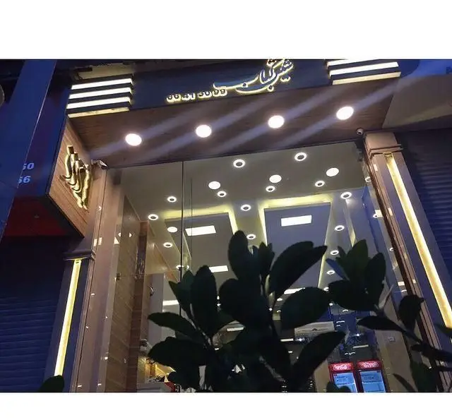 تصویری از نمای بیرونی شیک و نورانی رستوران شیش کباب در شب با تابلوی طلایی نئون و شماره تماس ۰۰۹۹۹۴۱۵۰۹۹، آماده خدمات‌رسانی.