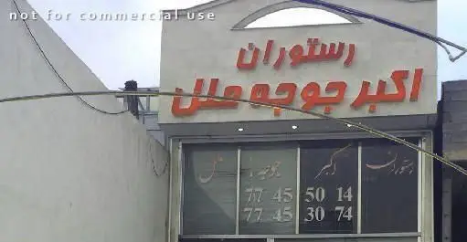 نمای بیرونی رستوران ایرانی اکبر جوجه ملل. تابلوی قرمز رنگ با حروف برجسته و شماره تلفن‌های قابل مشاهده روی شیشه برای رزرو و سفارش غذا.
