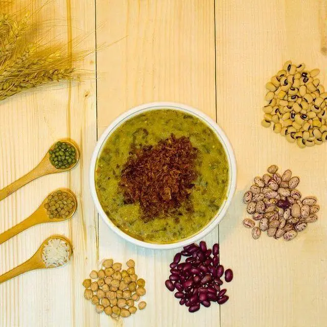 آش سنتی و خوشمزه آشکده دارچین، با تزئین پیاز داغ و مواد اولیه تازه شامل انواع حبوبات و غلات برای یک غذای سالم.