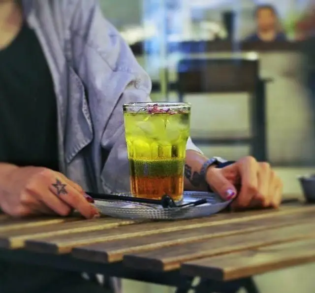 تجربه لذت‌بخش مشتری از نوشیدنی سرد و لایه‌ای با یخ و گل رز در فضای آرام و زیبای کافه مان و رو