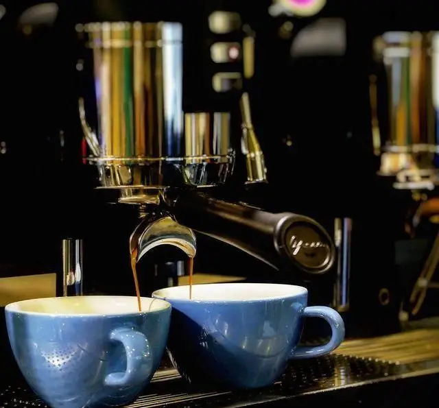 قهوه تازه و خوش عطر در حال عصاره گیری از دستگاه اسپرسو پیشرفته در کافه مان و رو به فنجان‌های آبی زیبا. کیفیت و طعم واقعی.