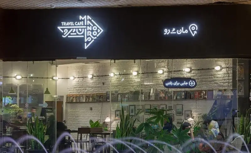 کافه مان و رو: نمای بیرونی و داخلی کافه سفر با نورپردازی زیبا، گیاهان و کتاب‌ها، فضایی دلنشین برای علاقه‌مندان به سفر.