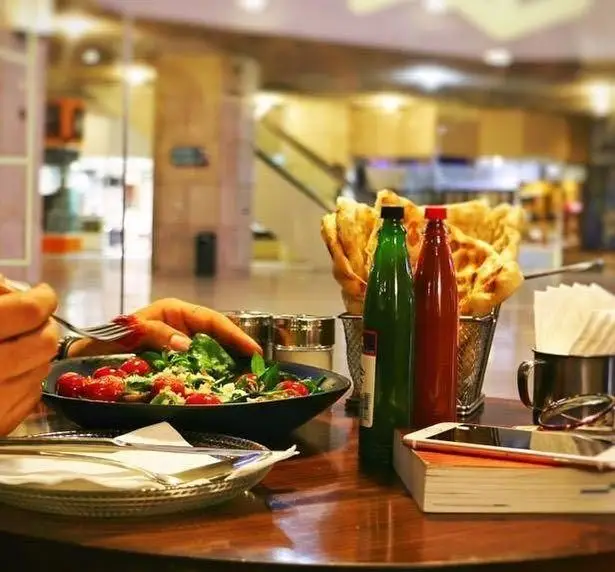 تجربه لذت‌بخش سرو سالاد تازه و نان داغ در کافه مان و رو. نمایی از میز غذاخوری با سس، شاکر و موبایل.