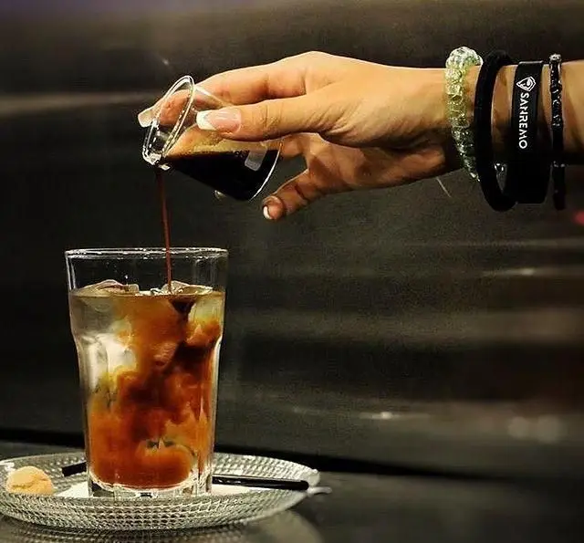 آماده سازی نوشیدنی سرد قهوه در کافه مان و رو: باریستا در حال ریختن اسپرسو روی یخ برای آیس کافی خنک و دلچسب