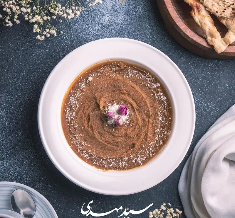 کاسه حلیم اصیل و خوش طعم سید مهدی، تزیین شده با پودر نارگیل و غنچه گل محمدی، در یک فضای سنتی و دلنشین.