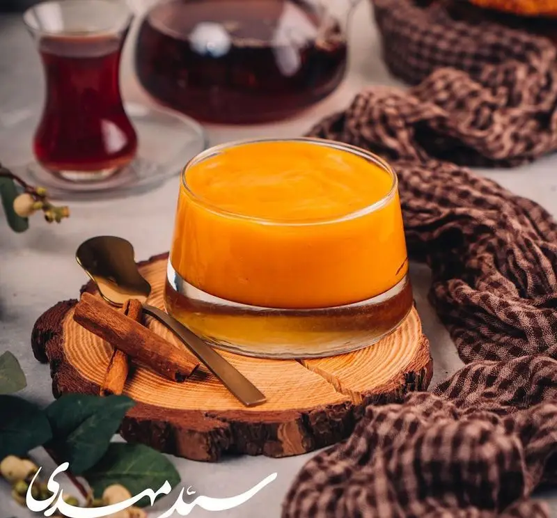 دسر یا نوشیدنی گرم و خوشرنگ سید مهدی، احتمالا کدو حلوایی، کنار چای داغ و دارچین، روی تخته چوبی. تجربه طعم‌های سنتی و اصیل.