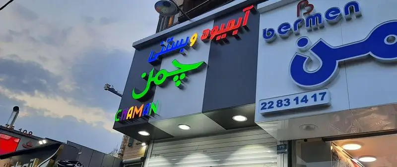 تابلو فروشگاه آبمیوه و بستنی چمن با لوگوی سبز رنگ در کنار مغازه برمن و شماره تلفن ۲۲۸۳۱۴۱۷ زیر آسمان ابری.