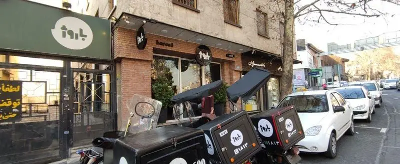 نمای بیرونی جذاب و مدرن فست فود باروژ با لوگوی بزرگ و واضح، به همراه موتورهای دلیوری آماده سرویس دهی در کنار خیابان