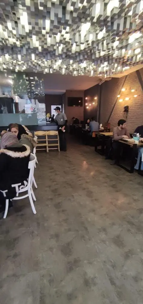 فضای داخلی مدرن و جذاب فست فود باروژ با سقف دکوراتیو منحصر به فرد و مشتریانی که از محیط دنج و غذای عالی لذت می‌برند.