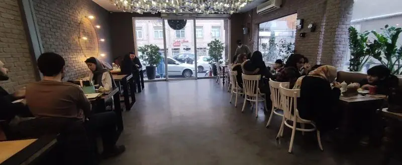 فضای داخلی دنج و مدرن فست فود باروژ با مشتریان شاد و در حال لذت بردن از غذا و نوشیدنی‌های متنوع، دیوارهای آجری و نورپردازی گرم و دلنشین.
