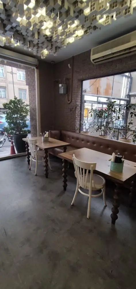 نمای داخلی مدرن و جذاب فست فود باروژ با دکوراسیون چوبی، نیمکت چرمی، صندلی‌های سفید و سقف مکعبی کنار پنجره.