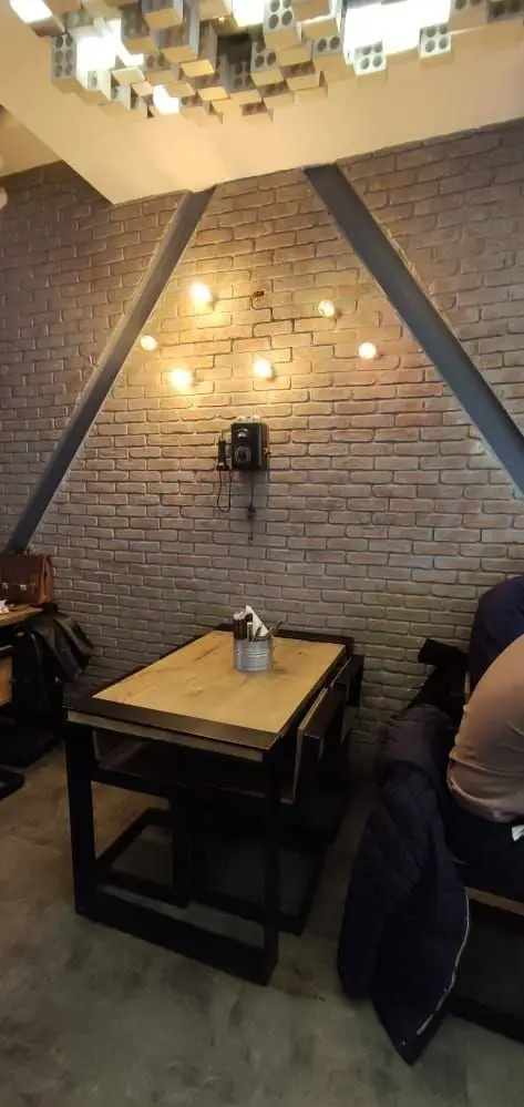 دکوراسیون داخلی فست فود باروژ: دیوار آجری، سقف با بلوک‌های تزئینی، میز چوبی، تلفن قدیمی دیواری، و نورپردازی گرم، محیطی جذاب و مدرن.