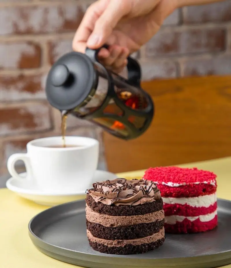 تصویری جذاب از کیک شکلاتی و ردولوت کنار یک فنجان چای تازه دم. لذت دسر و نوشیدنی‌های گرم در فست فود باروژ.