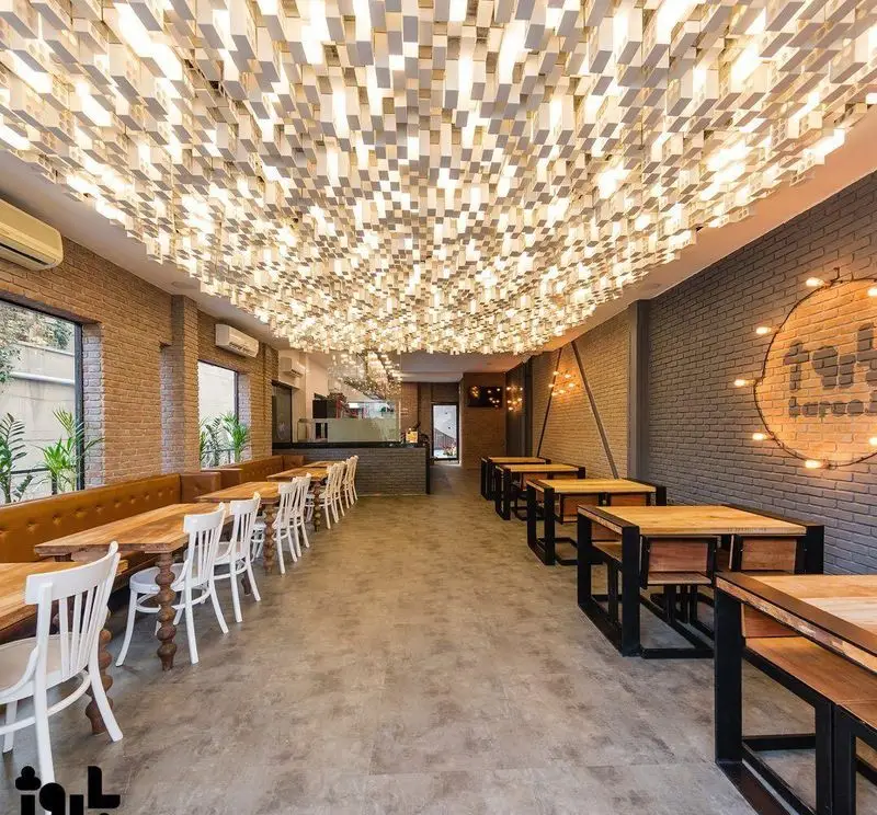 نمای داخلی فست فود باروژ: رستورانی با طراحی مدرن و نورپردازی خلاقانه سقفی، دیوارهای آجری، میز و صندلی چوبی و کاناپه‌های راحت.