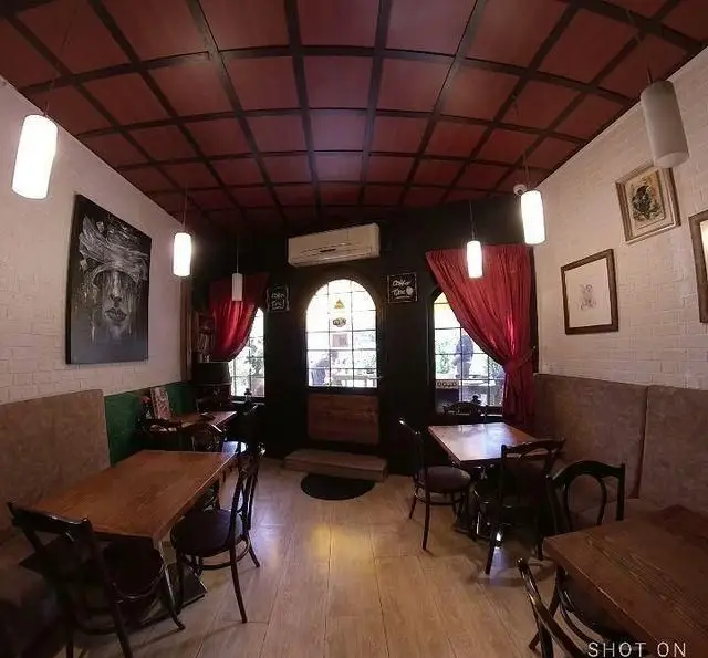 تصویری از فضای داخلی کافه آرکو با دکوراسیون کلاسیک، سقف مشبک قرمز، دیوارهای آجری سفید، میزهای چوبی و مبلمان راحت.
