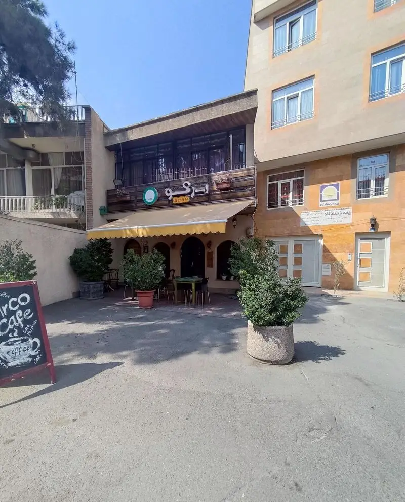 نمایی از کافه آرکو، کافه‌ای با فضای باز دلنشین، چتر آفتابگیر زرد و میز و صندلی‌ها. شماره تماس: ۲۲۲۲۳۱۹۴. مکانی ایده‌آل برای قهوه.