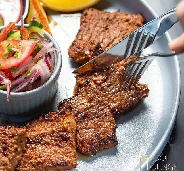 برش زدن کباب گریل شده یا استیک لذیذ در کافه رستوران روف لانژ (Rooflounge Cafe) با سالاد تازه. غذای خوشمزه و باکیفیت.