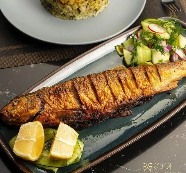 ماهی کبابی طلایی با سبزی پلو، سالاد تازه خیار و تربچه و لیموی تازه. غذای لذیذ دریایی در کافه رستوران روف لانژ.