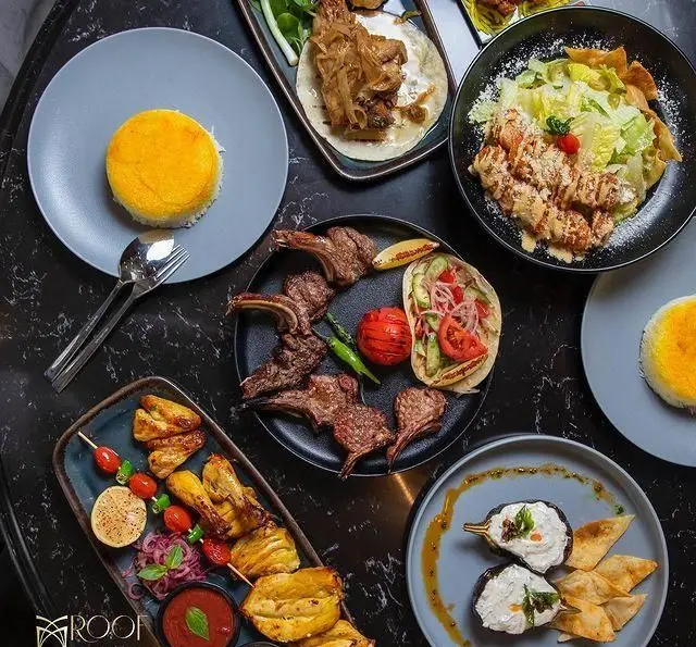 تصویری از میز رنگارنگ غذاهای ایرانی کافه رستوران روف لانژ: شیشلیک، جوجه کباب، ته چین، سالاد سزار، بادمجان و کبابهای دیگر.