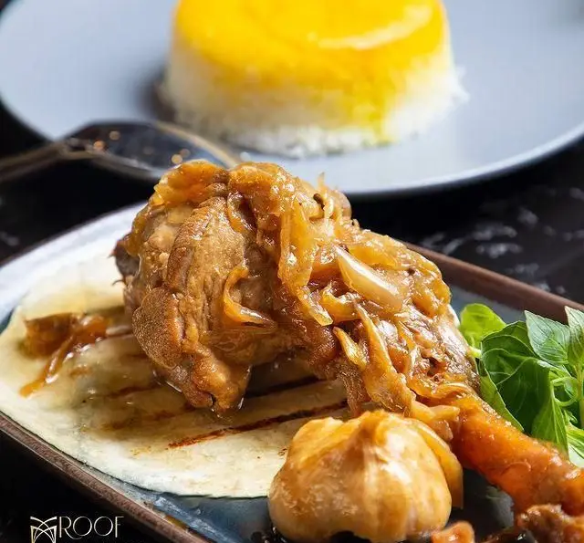 ران مرغ لذیذ با پیاز داغ طلایی، نان تازه و سیر در کافه رستوران روف لانژ. پلو زعفرانی در پس زمینه، تجربه‌ای شیک و منحصر به فرد.