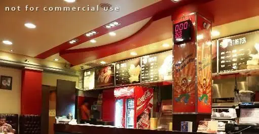 نمای داخلی پر جنب و جوش فست فود شایلی با پیشخوان آماده سازی، منوی متنوع غذا، یخچال نوشیدنی و محیطی دلپذیر برای مشتریان.