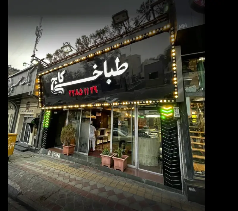 تصویری از نمای بیرونی و تابلوی طباخی کاج، متخصص کله پاچه با نورپردازی زیبا و شماره تماس ۲۲۸۵۱۱۴۲.