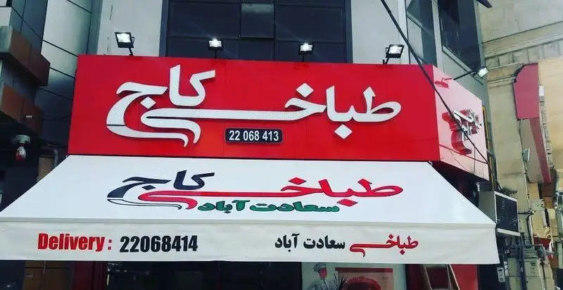 تصویری از نمای خارجی طباخی کاج در سعادت آباد، شامل تابلوی روشن و آویز با شماره تلفن 22068413 جهت سفارش آنلاین کله‌پاچه و تحویل سریع.