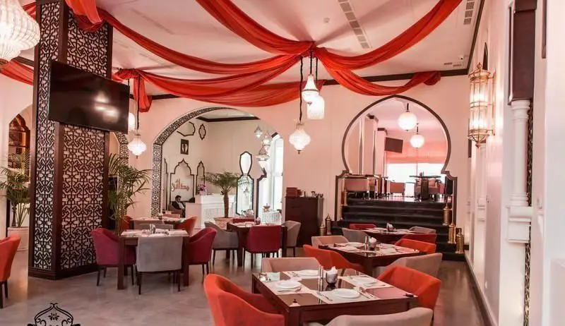 فضای داخلی لوکس کافه رستوران عربی مدائن با دکوراسیون سنتی، پرده‌های قرمز، میز و صندلی‌های شیک و نورپردازی دلنشین برای تجربه‌ای خاص.