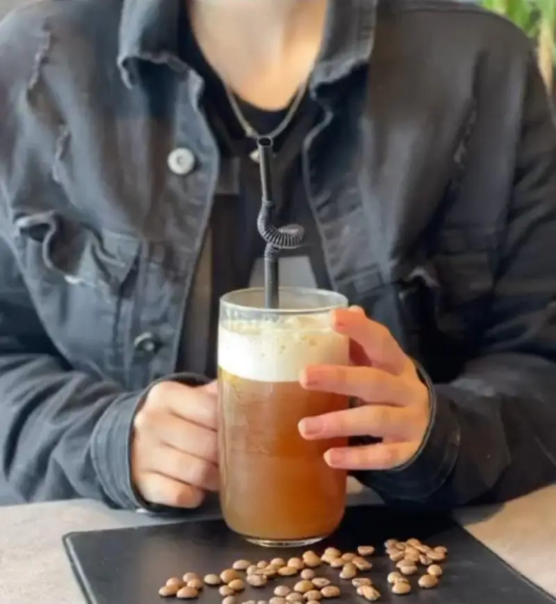 نوشیدنی خنک قهوه در کافه بیلیارد پلن بی، با فوم خامه‌ای و دانه‌های قهوه روی میز. تجربه‌ای دلچسب و فضایی دلنشین برای کافه‌گردی.