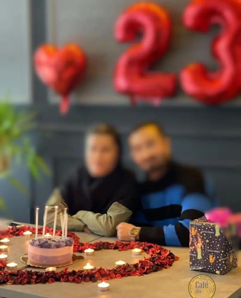 جشن تولد عاشقانه یک زوج در کافه بیلیارد پلن بی با دکوراسیون رمانتیک شامل بادکنک‌های ۲۳، کیک تولد، شمع و گلبرگ‌های قرمز، لحظه‌ای به‌یادماندنی.