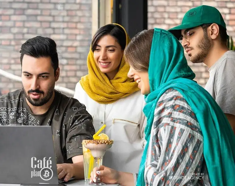 جوانان در کافه بیلیارد پلن بی دور هم جمع شده‌اند، یکی با لپ‌تاپ کار می‌کند و بقیه با علاقه به صفحه آن نگاه می‌کنند. این فضا نشان‌دهنده دورهمی و تعامل است.