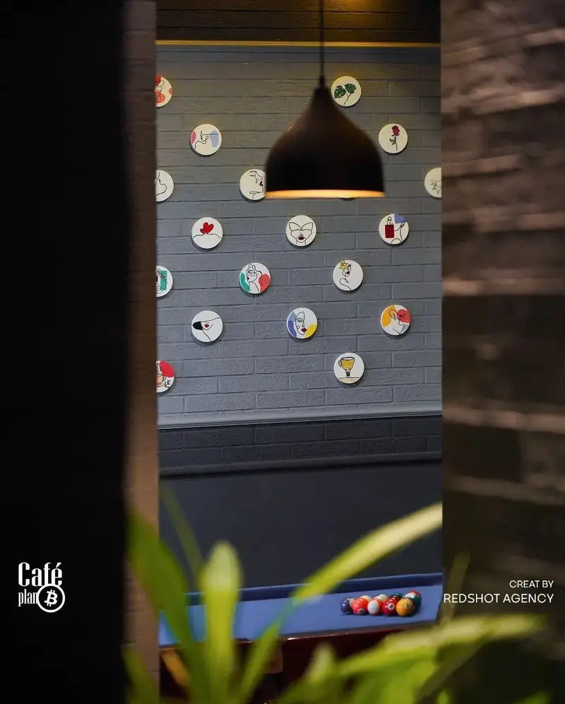 دکوراسیون داخلی کافه بیلیارد پلن بی با دیوار آجری خاکستری، بشقاب‌های تزئینی و میز بیلیارد. نورپردازی جذاب فضا.