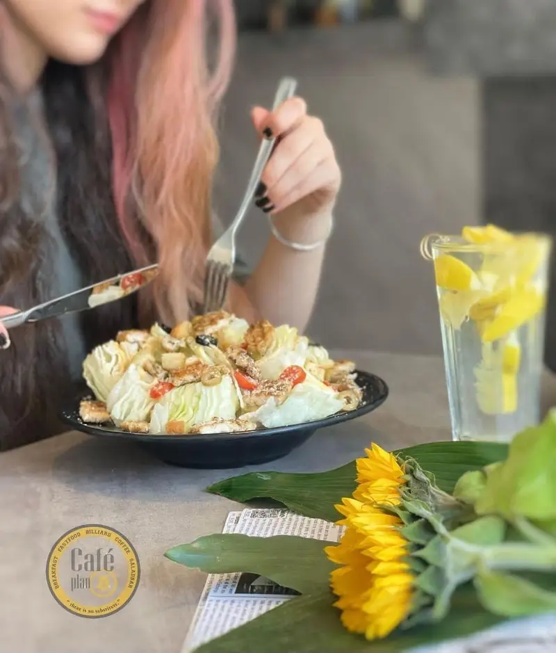 مشتری در کافه بیلیارد پلن بی سالاد خوش طعم شامل کاهو، گردو و زیتون را با چنگال و چاقو میل میکند، کنار آن آبلیمو و گل آفتابگردان است.