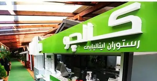 نمایی از ورودی رستوران ایتالیایی کالچو با تابلوی سبز رنگ و نام Calcio. محیطی دلنشین با سقف چوبی و دکوراسیون مدرن، ارائه دهنده غذاهای لذیذ ایتالیایی.