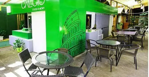 رستوران ایتالیایی کالچو: نمای فضای باز با دیوار سبز، میز و صندلی‌های شیک، و طرح کولوسئوم، محیطی دلنشین برای غذای اصیل ایتالیایی.
