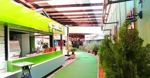 نمای دلباز از فضای باز رستوران ایتالیایی کالچو، با کیوسک سبز مدرن، مسیر چمن، و نورپردازی گرم برای تجربه‌ای دلپذیر.