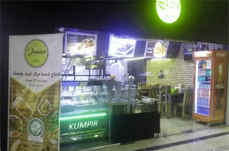 نمای خارجی ساندویچی دومان دنر، شعبه مرکز خرید ولنجک، با تابلوهای منو شامل کومپیر و کونفه و یخچال نوشیدنی‌های متنوع.