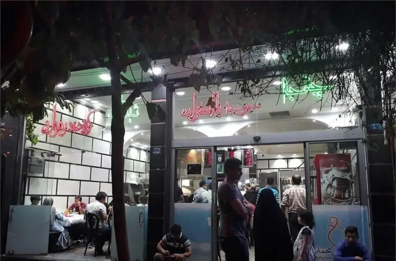 نمای بیرونی شبانه رستوران محمد با نورپردازی نئون چشمگیر، مشتریان داخل و خارج، و فضای پررونق یک مکان محبوب غذاخوری.
