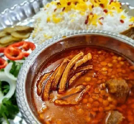 نمایی از خورش قیمه با ته دیگ سیب‌زمینی و برنج زعفرانی کنار سالاد و ترشی؛ لذت تجربه غذای اصیل ایرانی در کبابخانه دوزلی شعبه صادقیه.