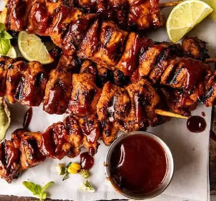 جوجه کباب‌های آبدار و خوشمزه دوزلی صادقیه با سس باربیکیو تیره و برش‌های لیمو تازه، آماده سرو در کبابخانه دوزلی.