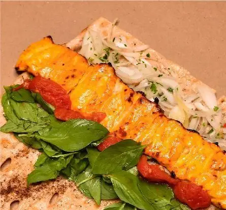 تصویری جذاب از جوجه کباب طلایی و لذیذ کبابخانه دوزلی شعبه صادقیه، سرو شده روی نان تازه با ریحان معطر و پیاز.