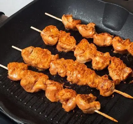 تصویری نزدیک از کباب جوجه‌های زعفرانی و لذیذ کبابخانه دوزلی شعبه صادقیه در حال گریل شدن روی تابه چدنی.