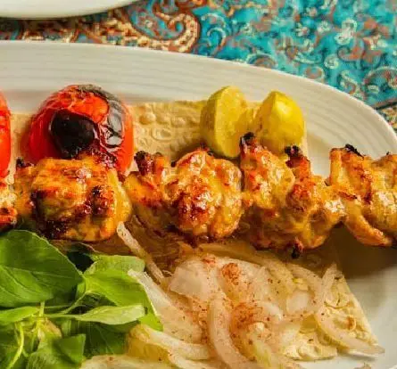 تصویری جذاب از جوجه کباب لذیذ با گوجه کبابی، پیاز، لیمو و سبزیجات تازه. بهترین غذای ایرانی در کبابخانه دوزلی شعبه صادقیه.
