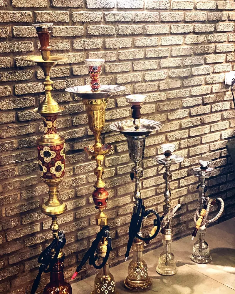 مجموعه‌ای متنوع از قلیان‌های برنجی و نقره‌ای با طرح‌های سنتی و زیبا در کافه عربی میر مهنا، مناسب برای تجربه‌ای اصیل.