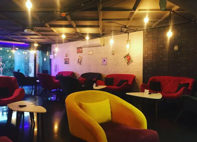 کافه دیاکو، فضایی شیک و مدرن با مبل‌های راحتی قرمز و زرد، دیوار آجری سفید، نورپردازی صنعتی و محیطی دلپذیر برای کافه‌نشینی و دورهمی.