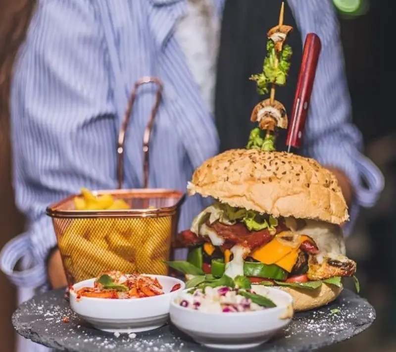 برگر بزرگ و اشتها آور کافه دیاکو با نان کنجدی، بیکن، پنیر و سبزیجات تازه، همراه سیب زمینی سرخ کرده و سالادهای ویژه.