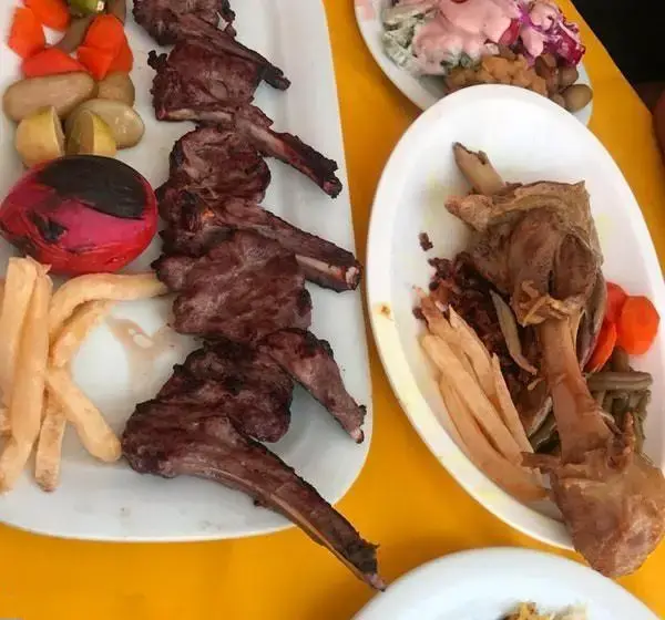 سفره‌ای رنگین از غذاهای لذیذ رستوران باغ بهشت: شیشلیک آبدار، گردن گوسفندی، سیب‌زمینی سرخ‌کرده و ترشیجات تازه. لذت طعم اصیل ایرانی.